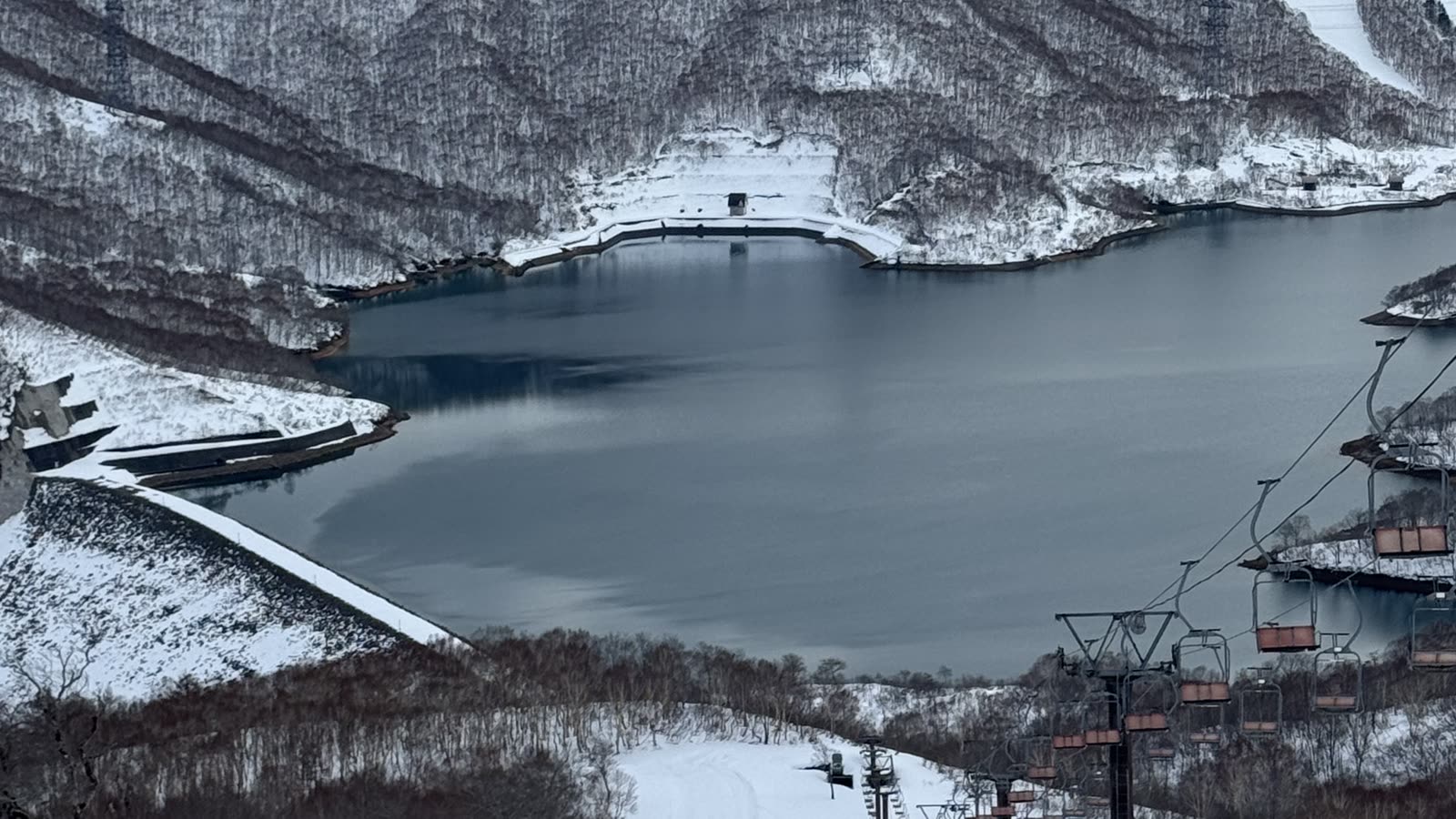從神樂滑雪場高處俯瞰雪道與湛藍的田代湖,遠方雪山層疊
