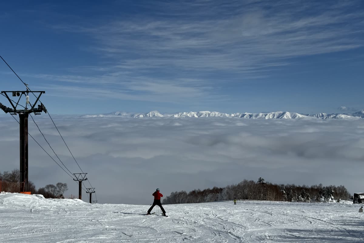 三位滑雪與單板玩家在雪道中段轉彎下滑,背景是田代湖與遠山